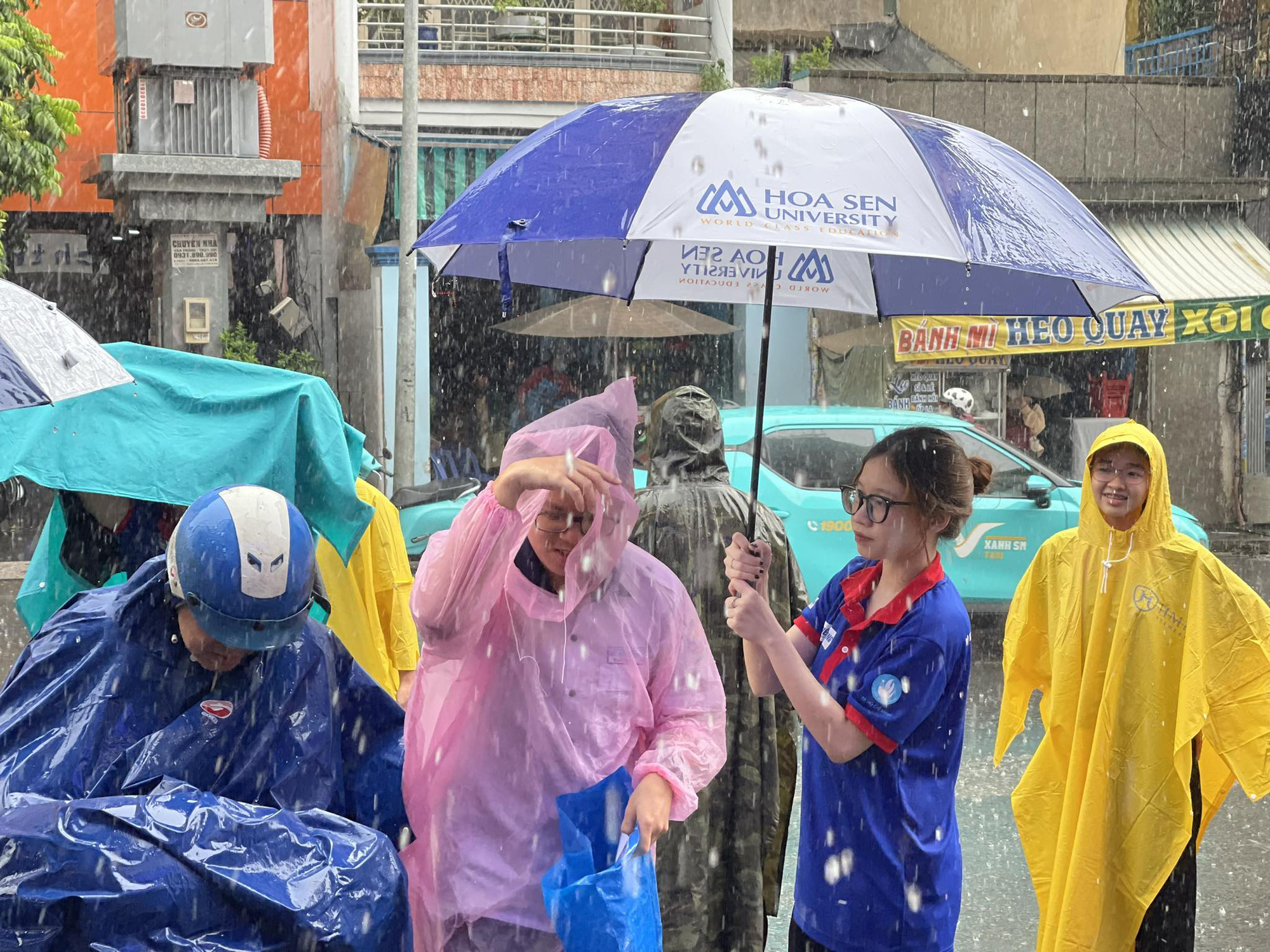 TP.HCM và nhiều nơi mưa to, thí sinh đi thi chú ý- Ảnh 3. Một số nơi ở TP.HCM mưa lớn, thí sinh được tình nguyện viên che dù đưa vào điểm thi - Ảnh: LÊ THÀNH HUY