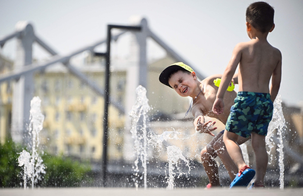 Thủ đô nước Nga nắng nóng nhất trăm năm qua- Ảnh 1. Trẻ em chơi đùa dưới đài phun nước trong nắng nóng ở trung tâm Mátxcơva vào ngày 3-7-2024 - Ảnh: AFP